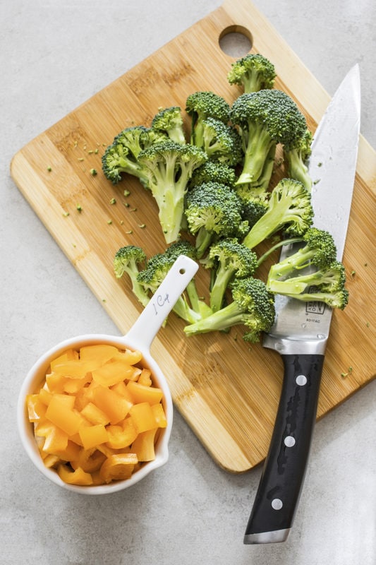 Broccoli and chopped peppers on a wooden cutting board