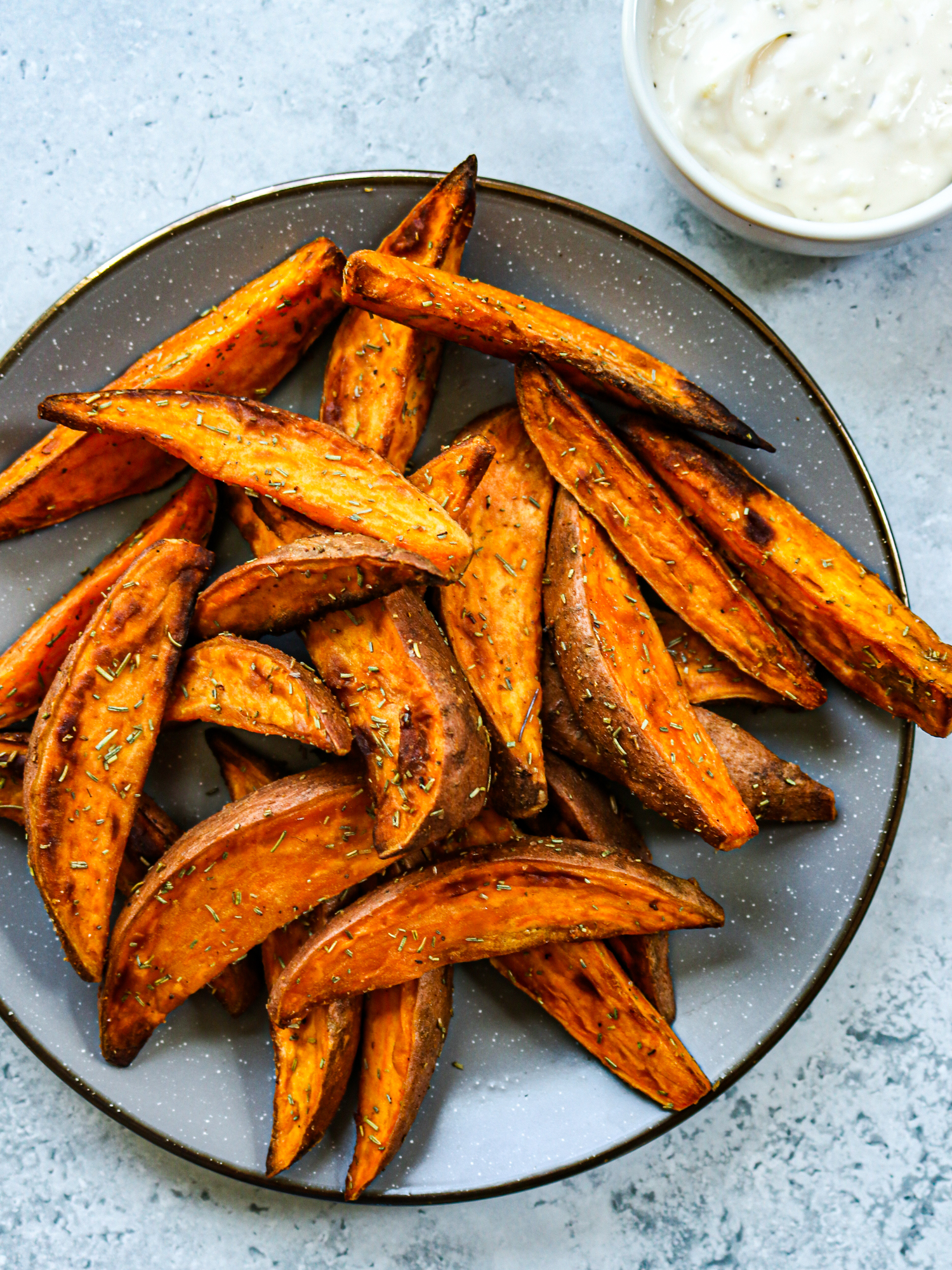 Air fryer sweet potato wedges on a plate with garlic aioli in a bowl